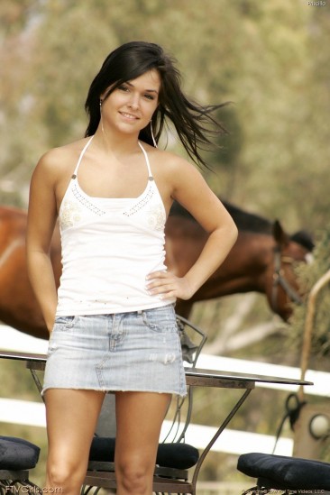 Sexy brunette doll Eden Petty in jeans skirt makes a strip show by a farm in the country